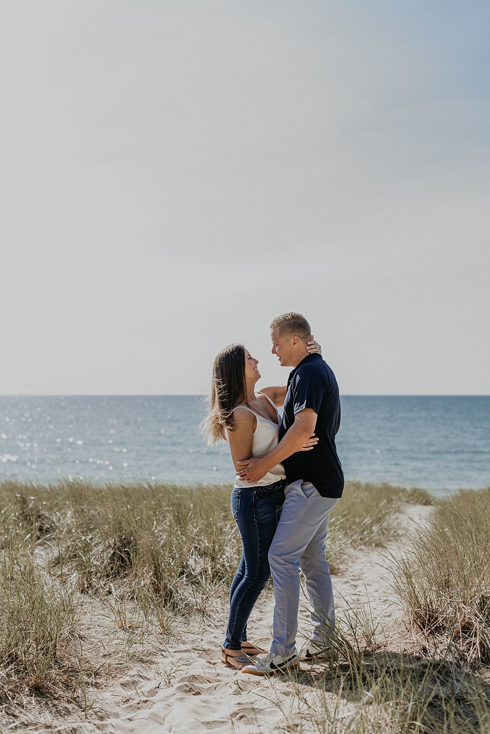 Engaged couple on the beach of Lake Michigan embracing while smiling at each other lovingly.